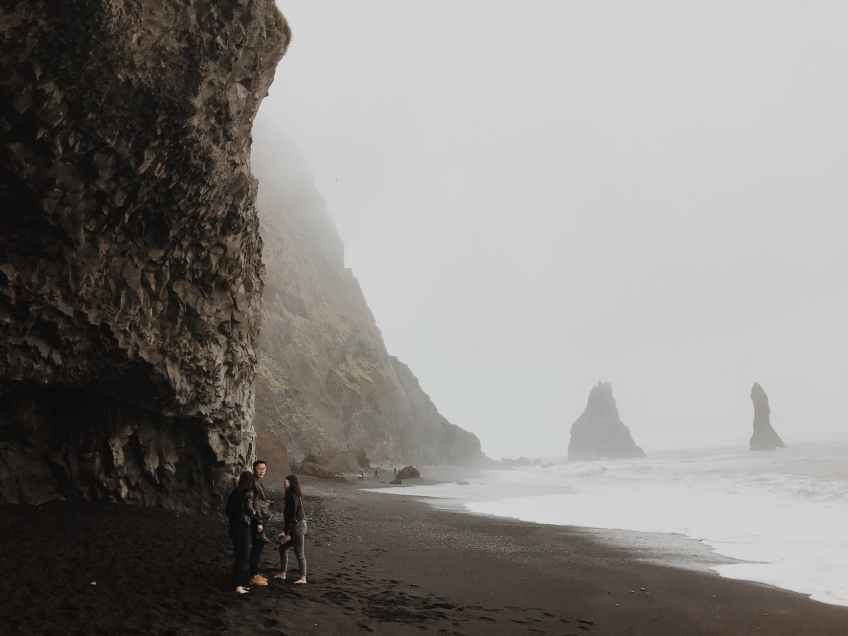 three people standing near seashore viewing cliff covered with fogs
